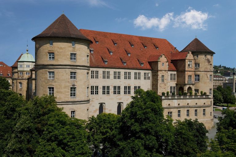 Altes Schloss in Stuttgart Historisches Schloss mit rotem Dach und grüner Kuppel, umgeben von Bäumen.