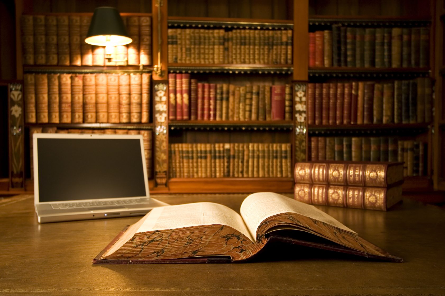 Aufgeschlagenes Buch in einer Bibliothek mit einem Laptop und Bücherregalen im Hintergrund.