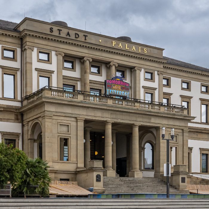 Historisches Palais mit Säulen und Eingangstreppe, unter grauem Himmel.